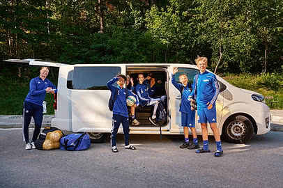 Ett ungdomslag i träningskläder står vid en minibuss inför avfärd till match eller turnering.